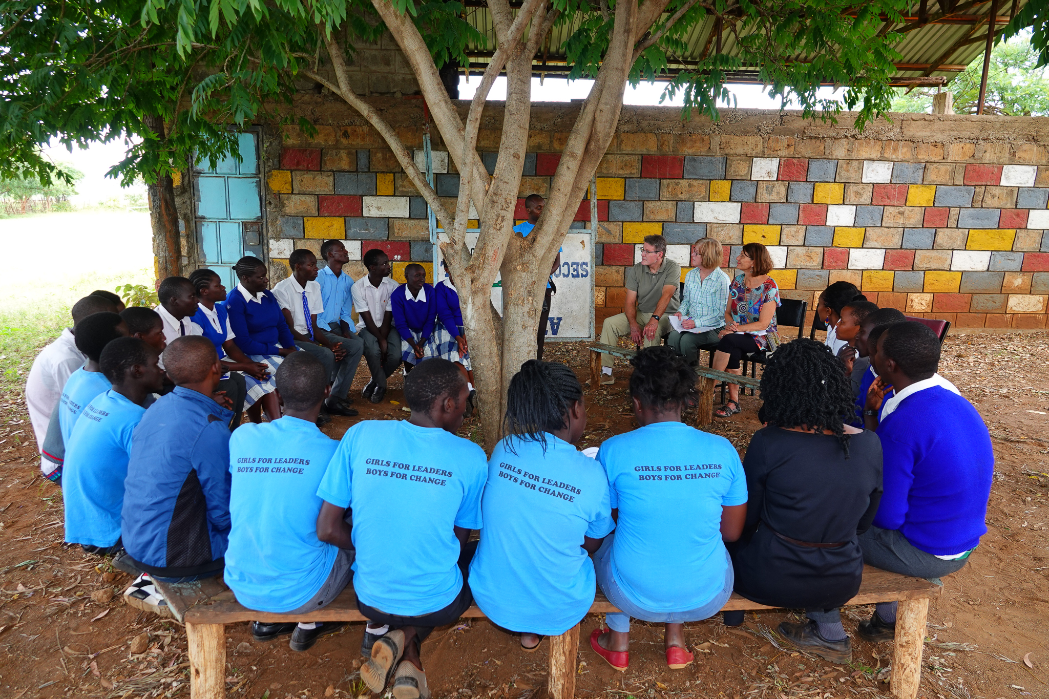 members site in a circle outdoors around a tree and hear from students from the girls for leaders program in Kenya.